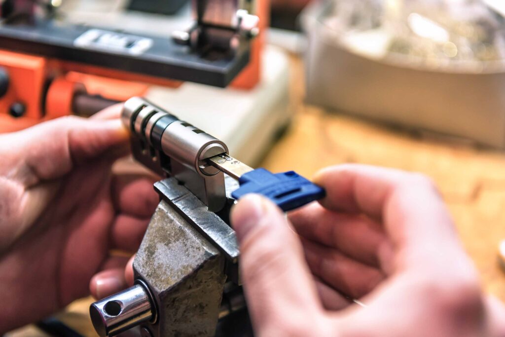 Close-up of hands working on a lock cylinder with a blue key inserted, held in a vise