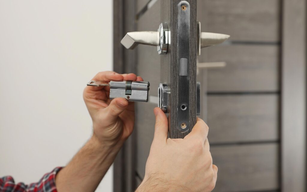 Person installing a door lock mechanism on a wooden door, focusing on the alignment of the lock cylinder and handle.