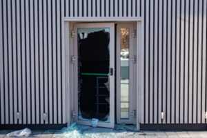 A broken glass door with shattered pieces scattered on the ground