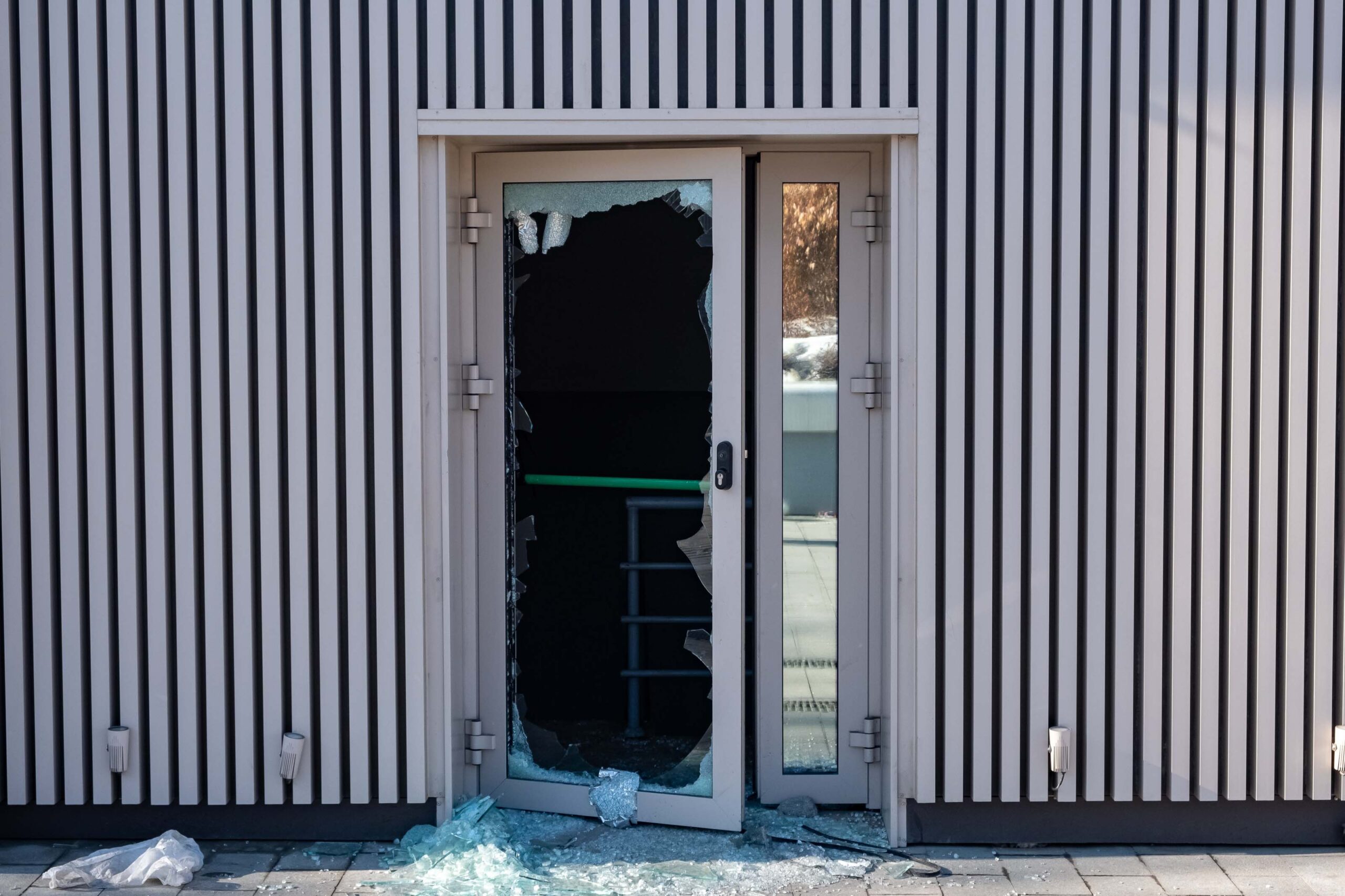 A broken glass door with shattered pieces scattered on the ground